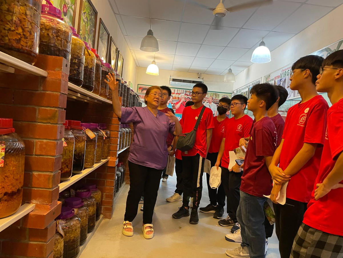 Shopkeeper showing students the different type of food in huge red glass jars on the shelf.